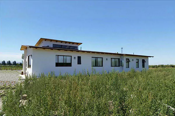 Una casa blanca con techo marrón, rodeada de hierba alta y verde y un camino de grava.