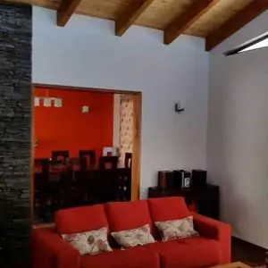 Un sofá rojo se encuentra en una habitación con una pared de piedra y vigas de madera en el techo