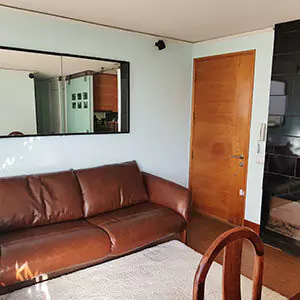 Un salón con un sofá de cuero marrón, un espejo en la pared y una puerta que da a otra habitación